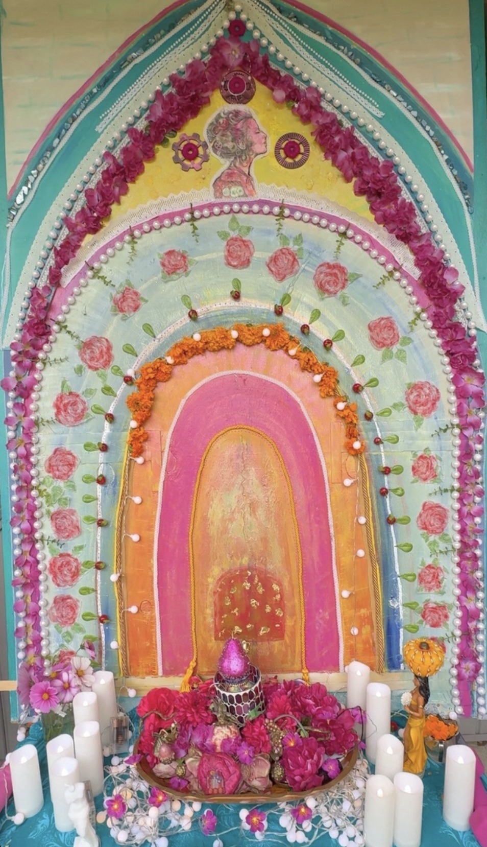 The hand-painted entrance to The House of Religare: a rose and teal archway of flowers, pearls, and marigolds standing above an altar of candles and roses
