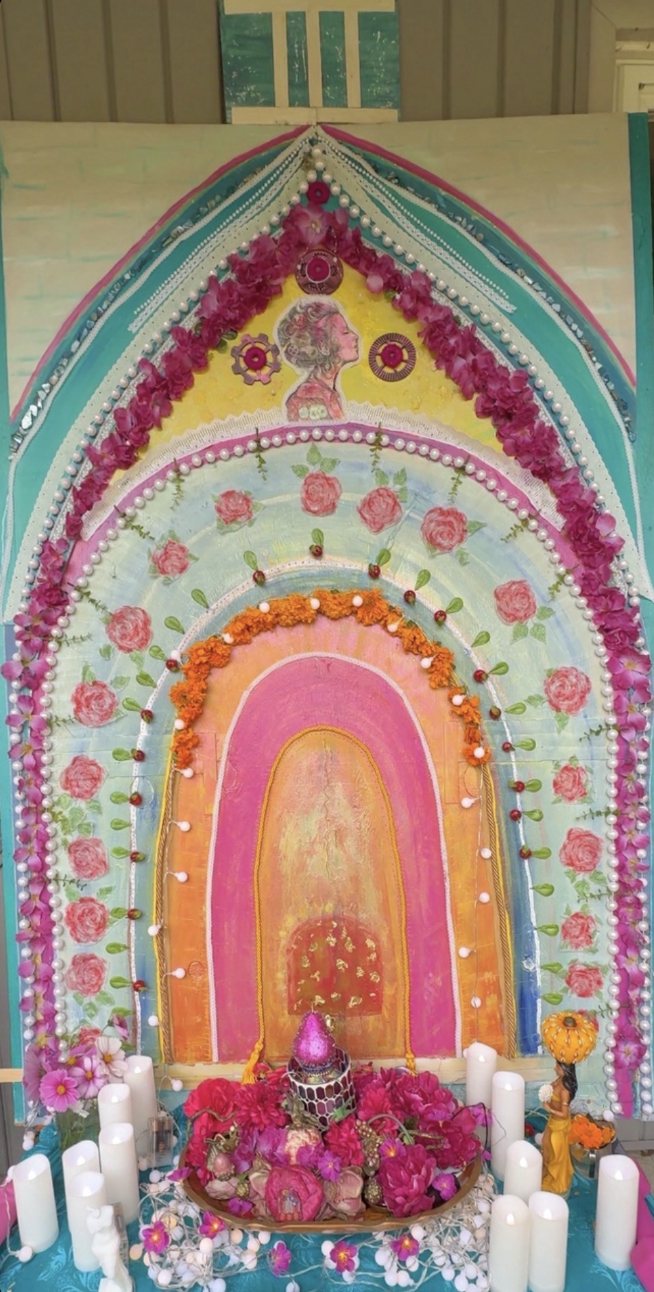 A handmade arched altar in rose, turquoise, and gold, adorned with flowers and candles