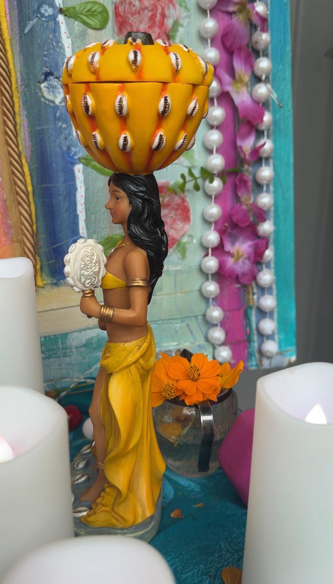 An Ochún figure in yellow with offerings, candles, and flowers
