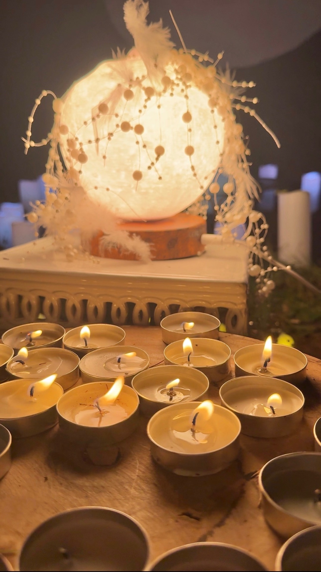 A glowing moon orb wrapped in white feathers and pearls above a field of candles