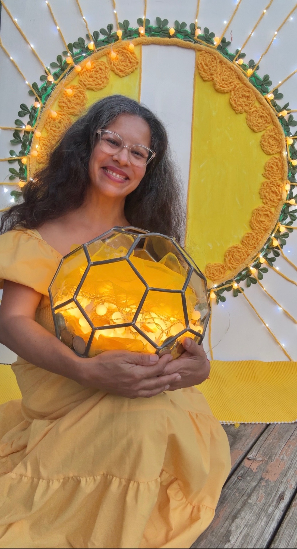 Mariela in yellow holding a glowing golden geometric sphere