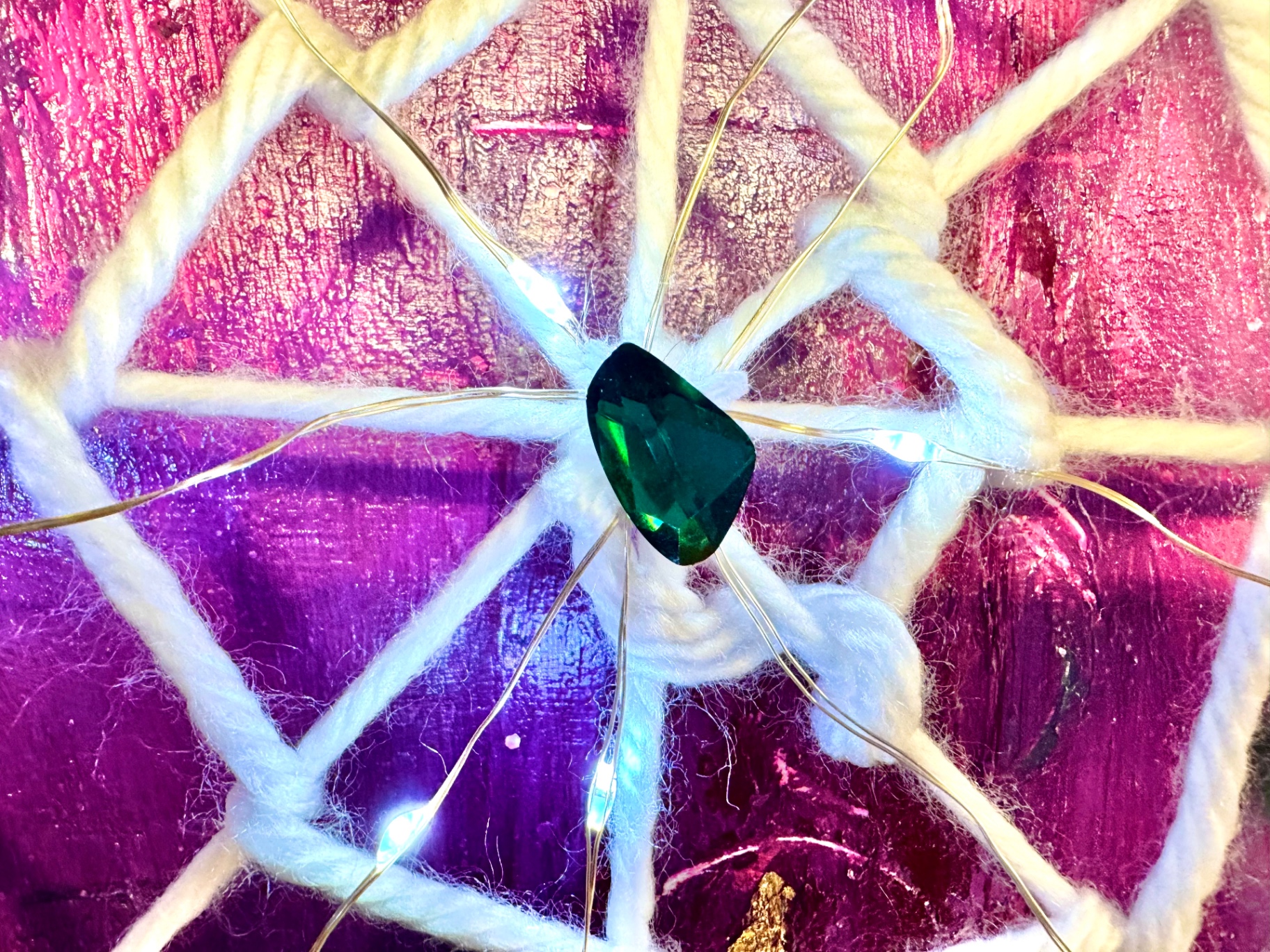 Close-up of a green jewel at the center of a woven web lit with tiny lights