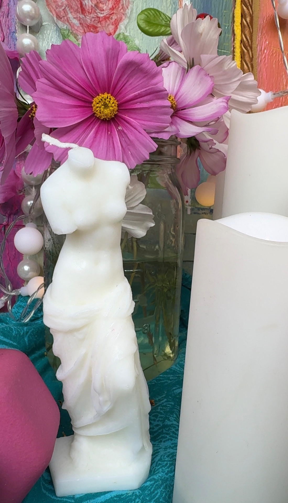 A Venus statue surrounded by cosmos flowers, candles, and altar objects