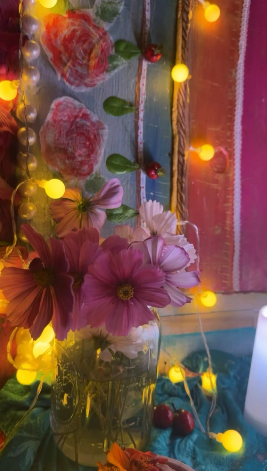 Pink cosmos flowers and warm lights before a colorful handmade altar